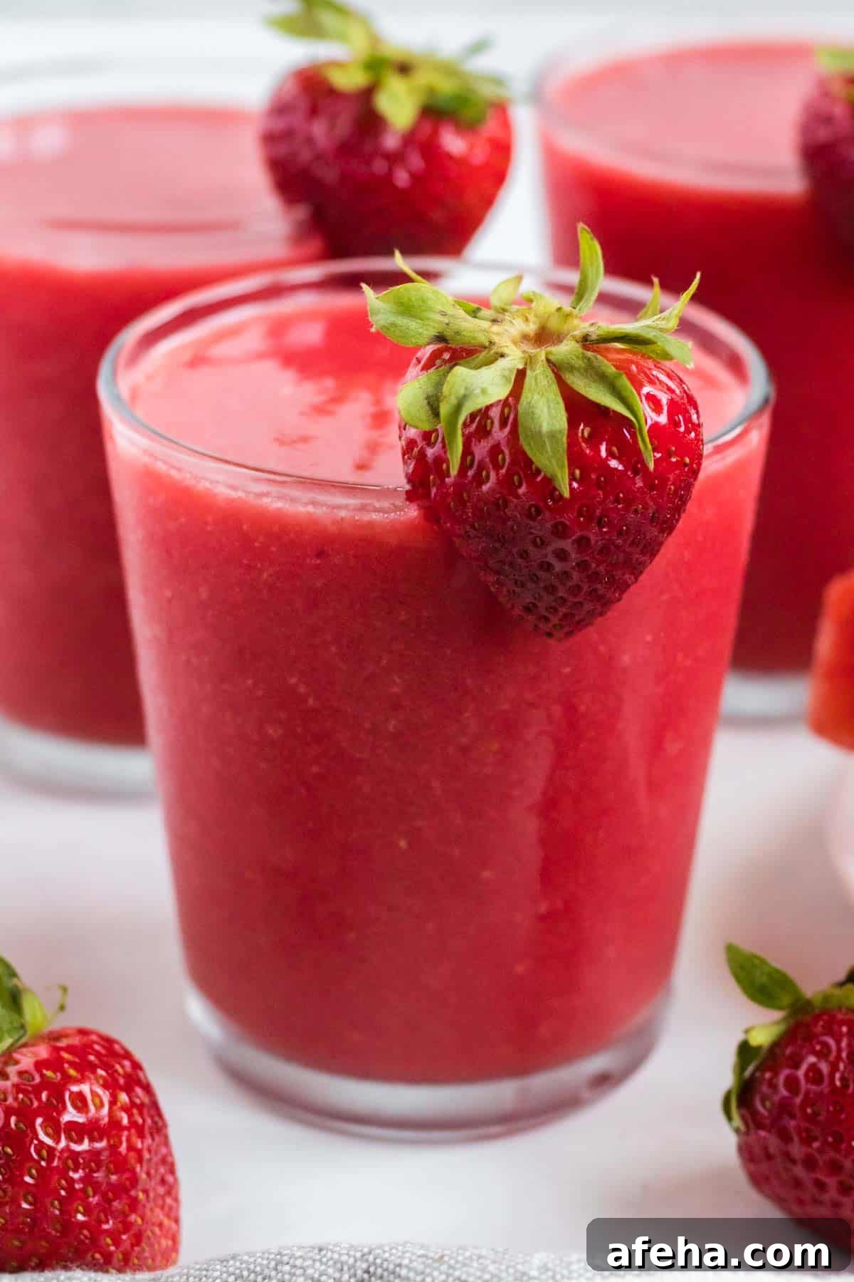 strawberry watermelon smoothie in a clear glass with a strawberry on the rim
