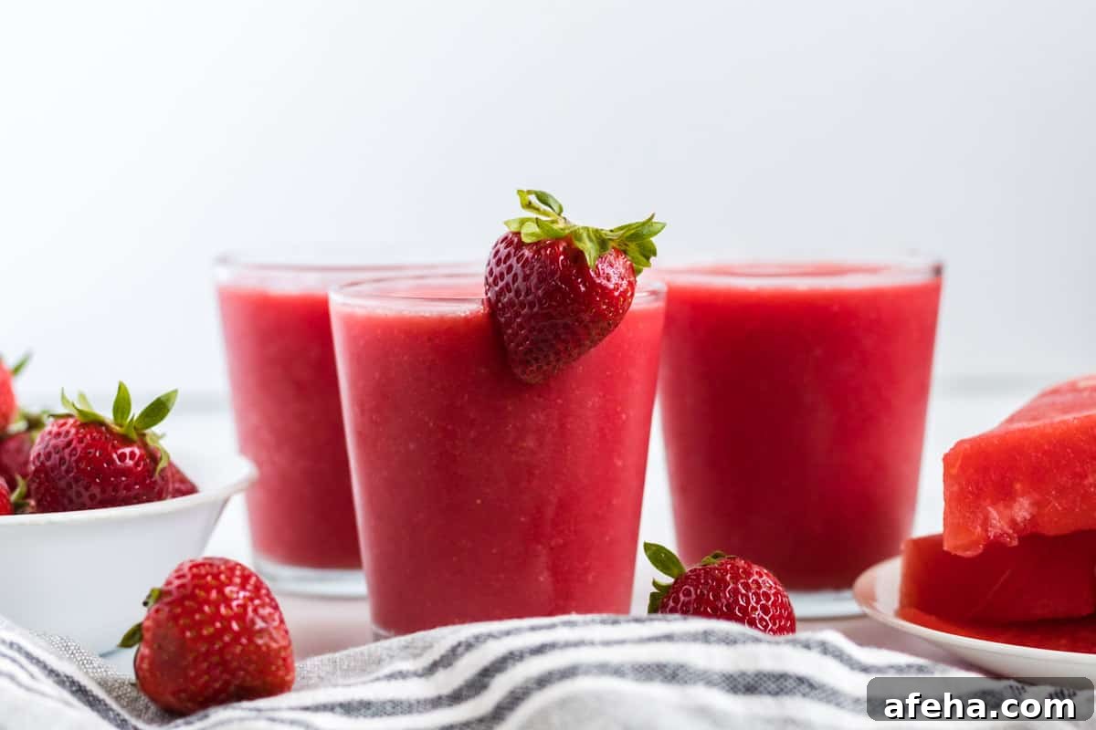 strawberry watermelon smoothie in a clear glass with a strawberry on the rim