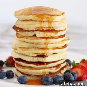 Tall stack of buttermilk pancakes with maple syrup and berries around. White background.