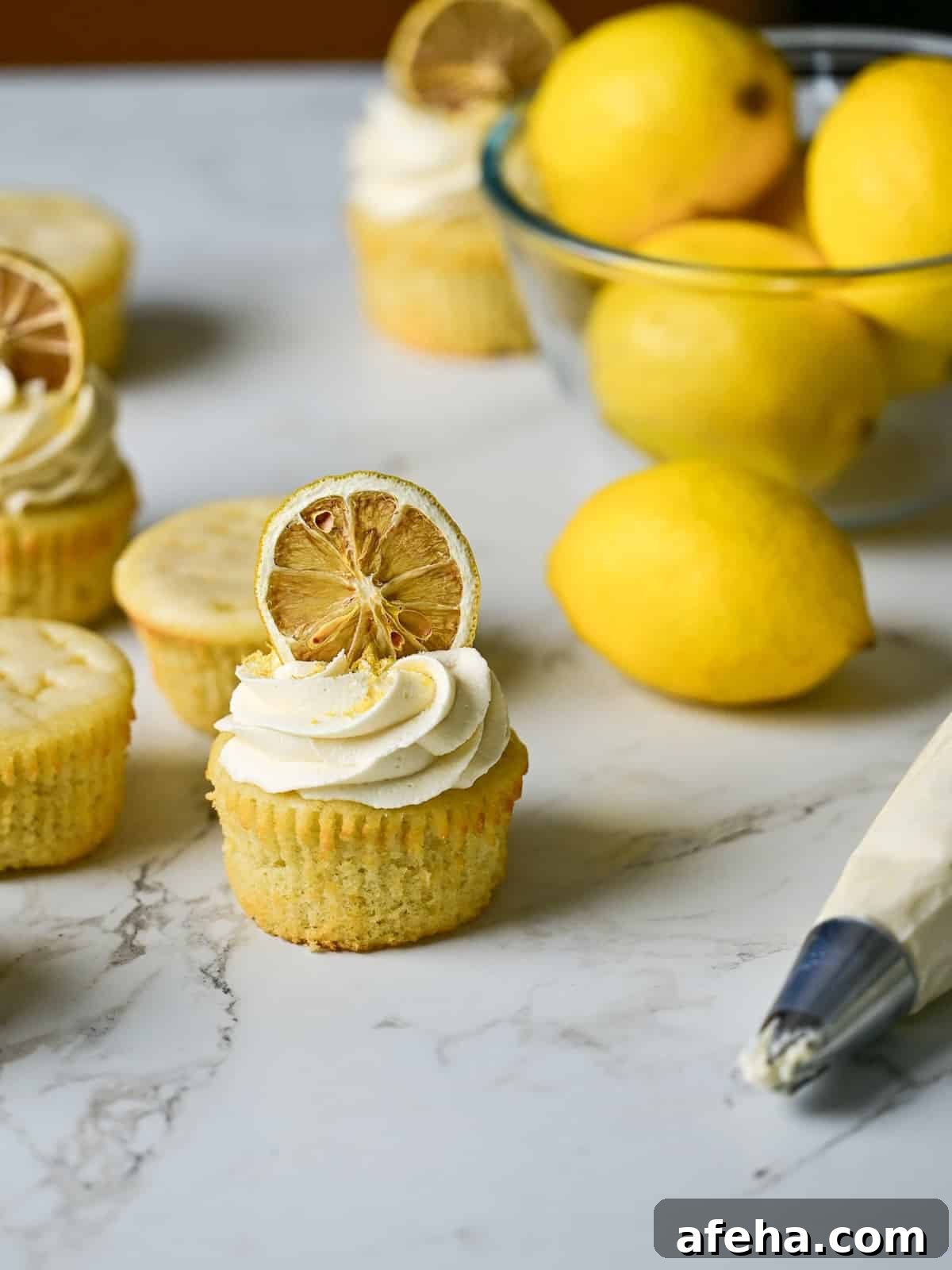 marble table with freshly made lemon drizzle cupcakes topped with frosting and dried lemon wheels.