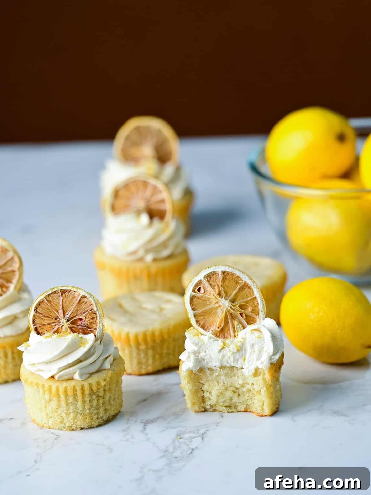 batch of lemon drizzle cupcakes with lemon frosting and dried lemon slices on top.