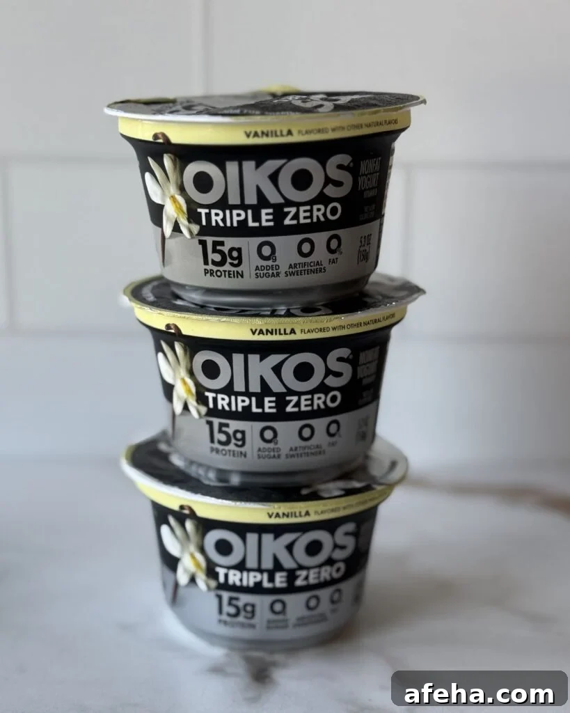 Three stacked vanilla Oikos triple zero yogurts on a countertop.