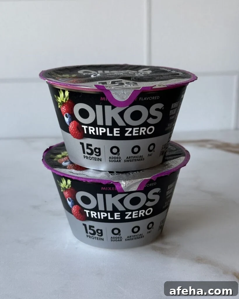 Two stacked berry Oikos triple zero yogurts on a countertop.