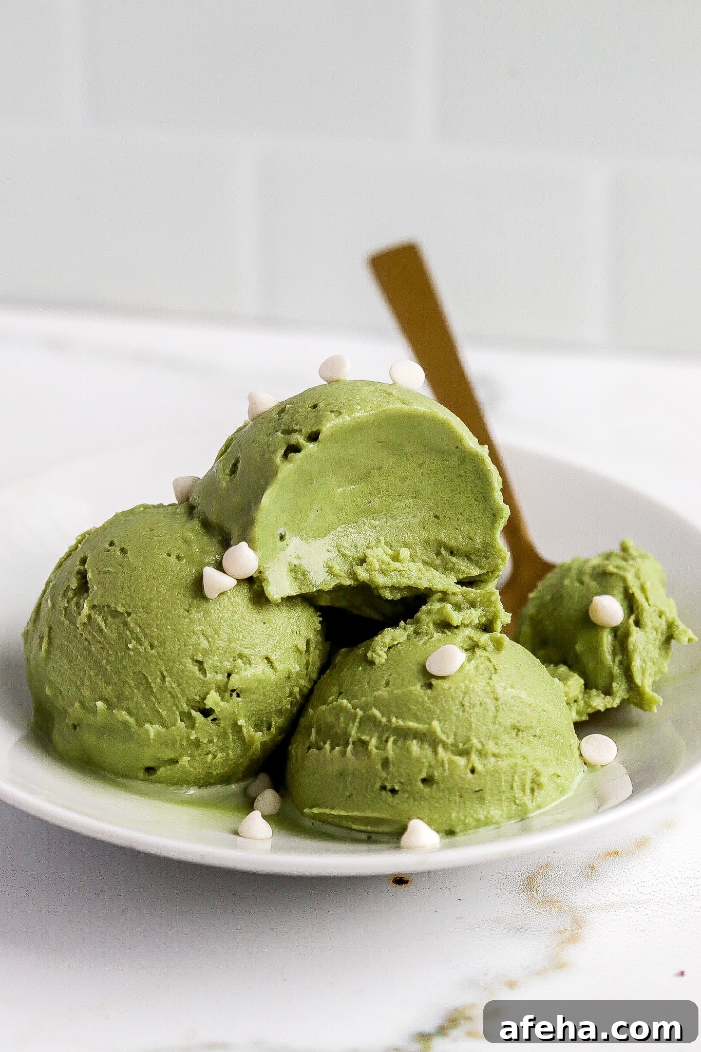 Ninja Creami Matcha Ice Cream: 48g Protein 6 Side view of matcha ice cream scoops in white bowl with gold spoon and mini white chocolate chips.
