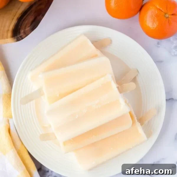 Orange popsicles on a white plate with oranges.
