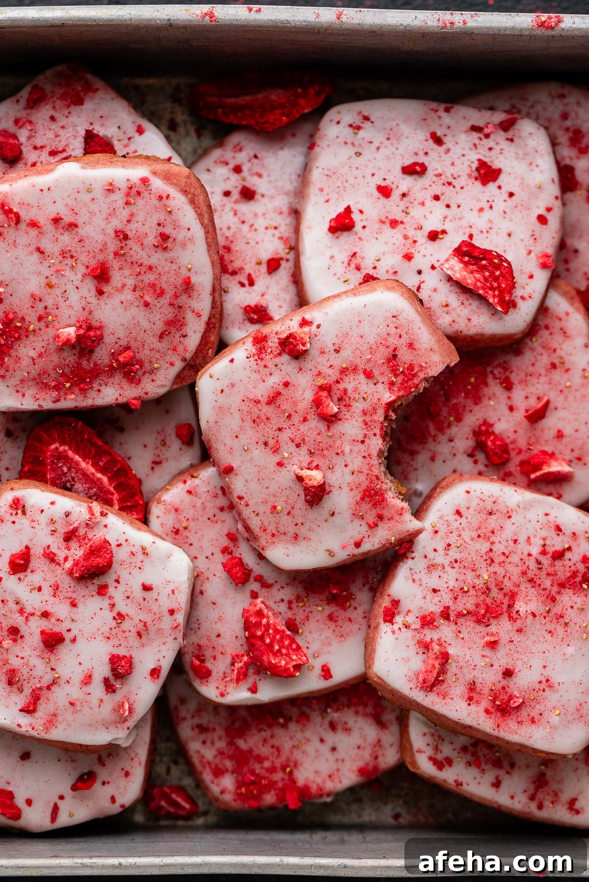 Strawberry shortbread cookies topped with a powdered sugar glaze and freeze dried strawberry bits randomly placed in a vintage baking tin.