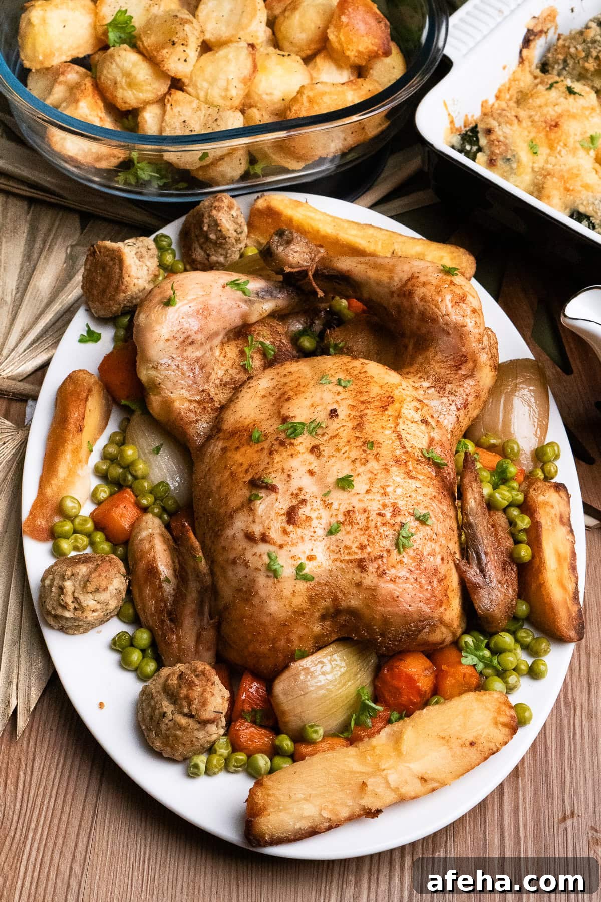 Slow cooker roast chicken served on a white platter plate with the carrots and onions it was cooked with, as well as all the trimmings, yorkshire puddings, parsnips,roast potatoes, stuffing and peas.