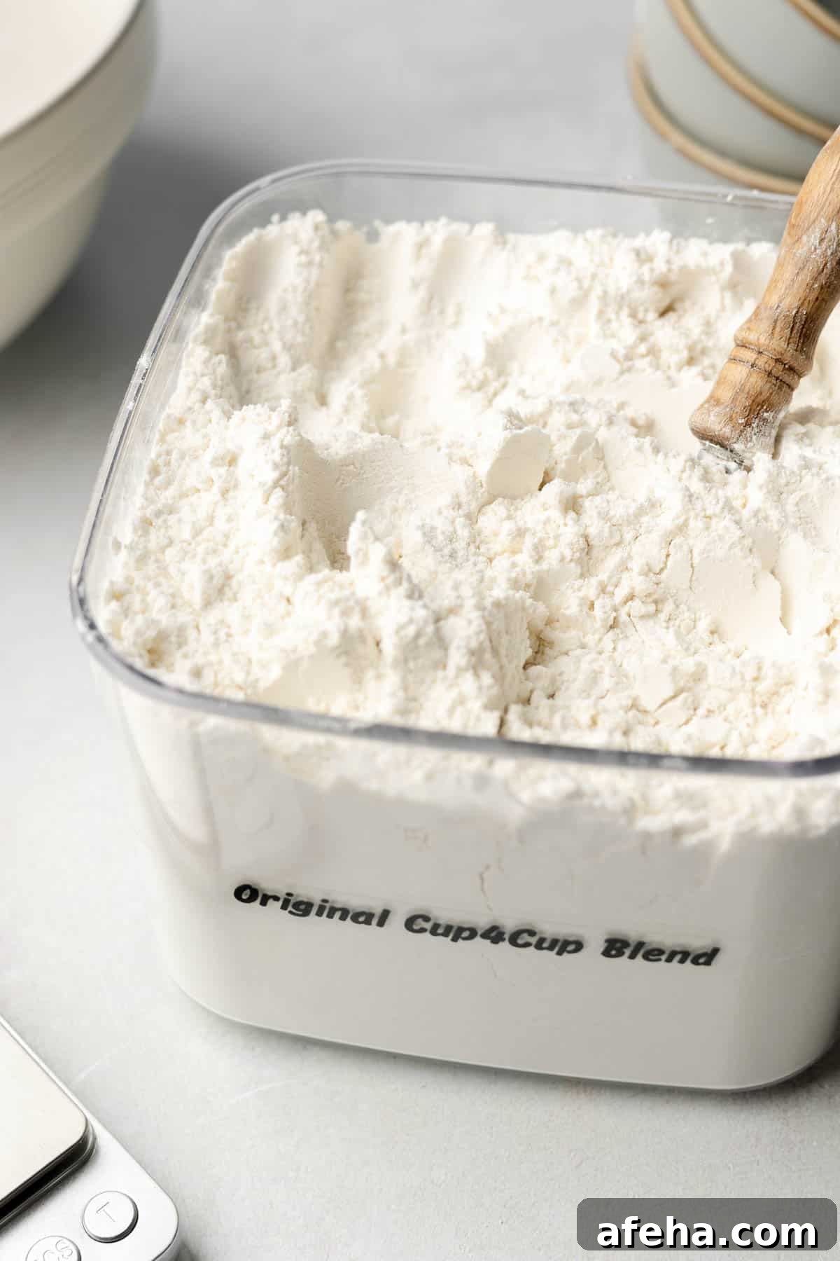 A bin filled with cup4cup gluten-free flour blend, wooden spoon handle sticking out. 