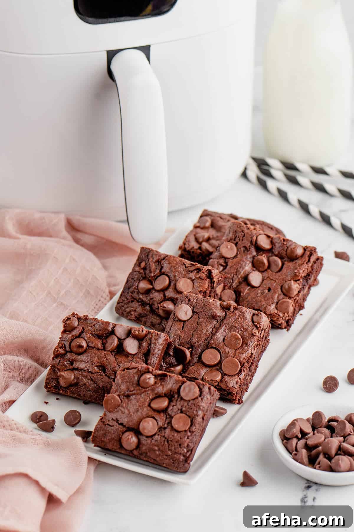 Six square pieces of brownies on a serving plate in front of an air fryer.