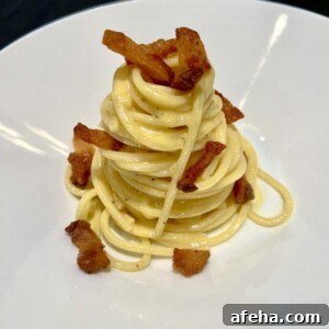 A plate of spaghetti carbonara is neatly presented in a swirl topped with crispy bacon pieces. The creamy pasta is lightly coated in sauce and garnished with black pepper, served on a white dish.