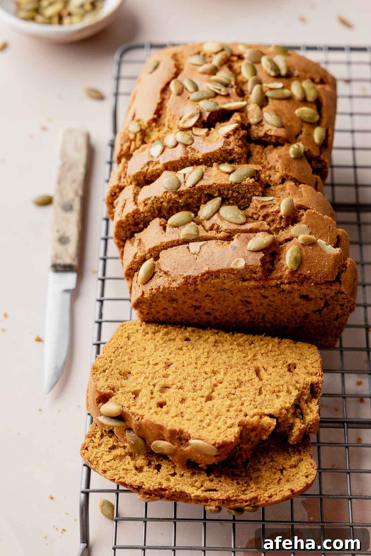Sliced gluten free pumpkin bread loaf with pumpkin seeds on wire rack.