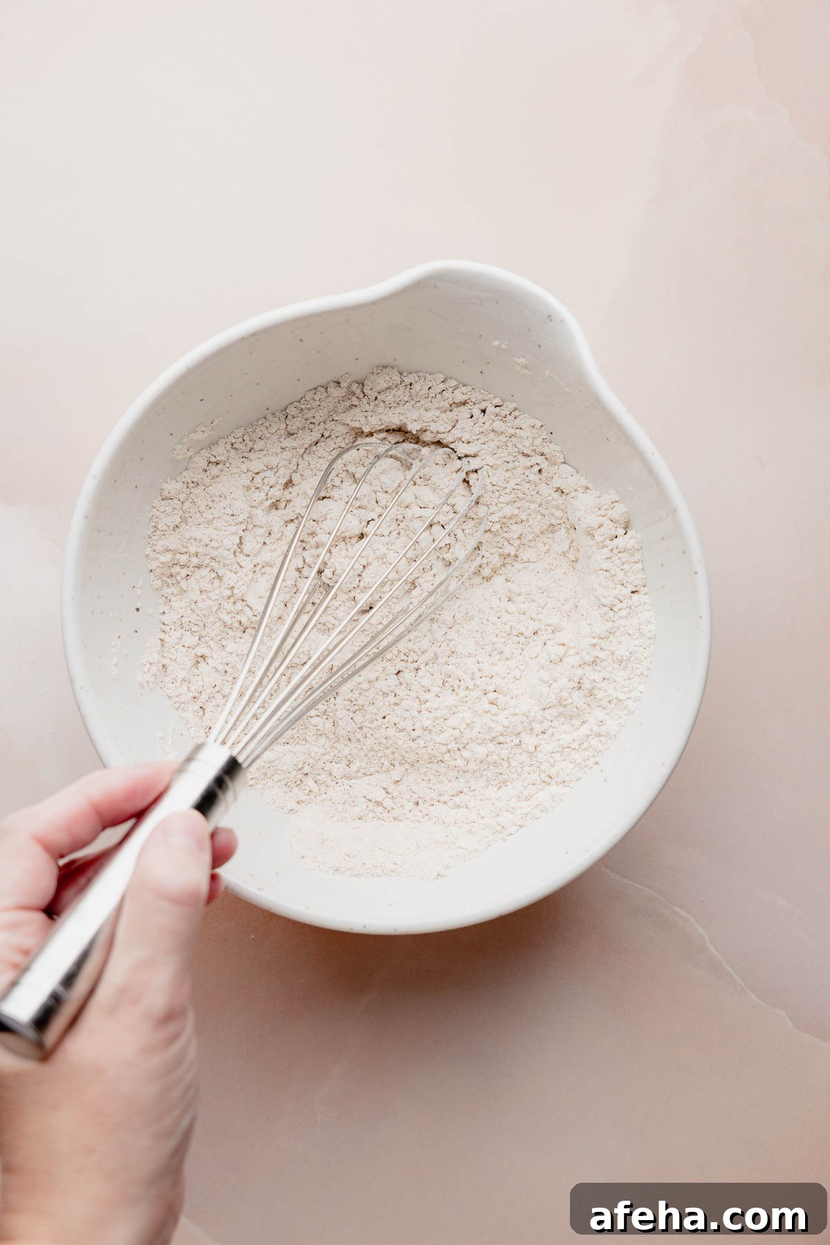 White bowl of flour mixture with whisk for gluten free pumpkin bread.