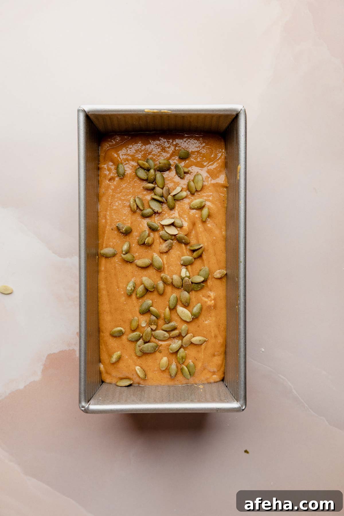 Gluten free pumpkin bread batter in loaf pan topped with pumpkin seeds.