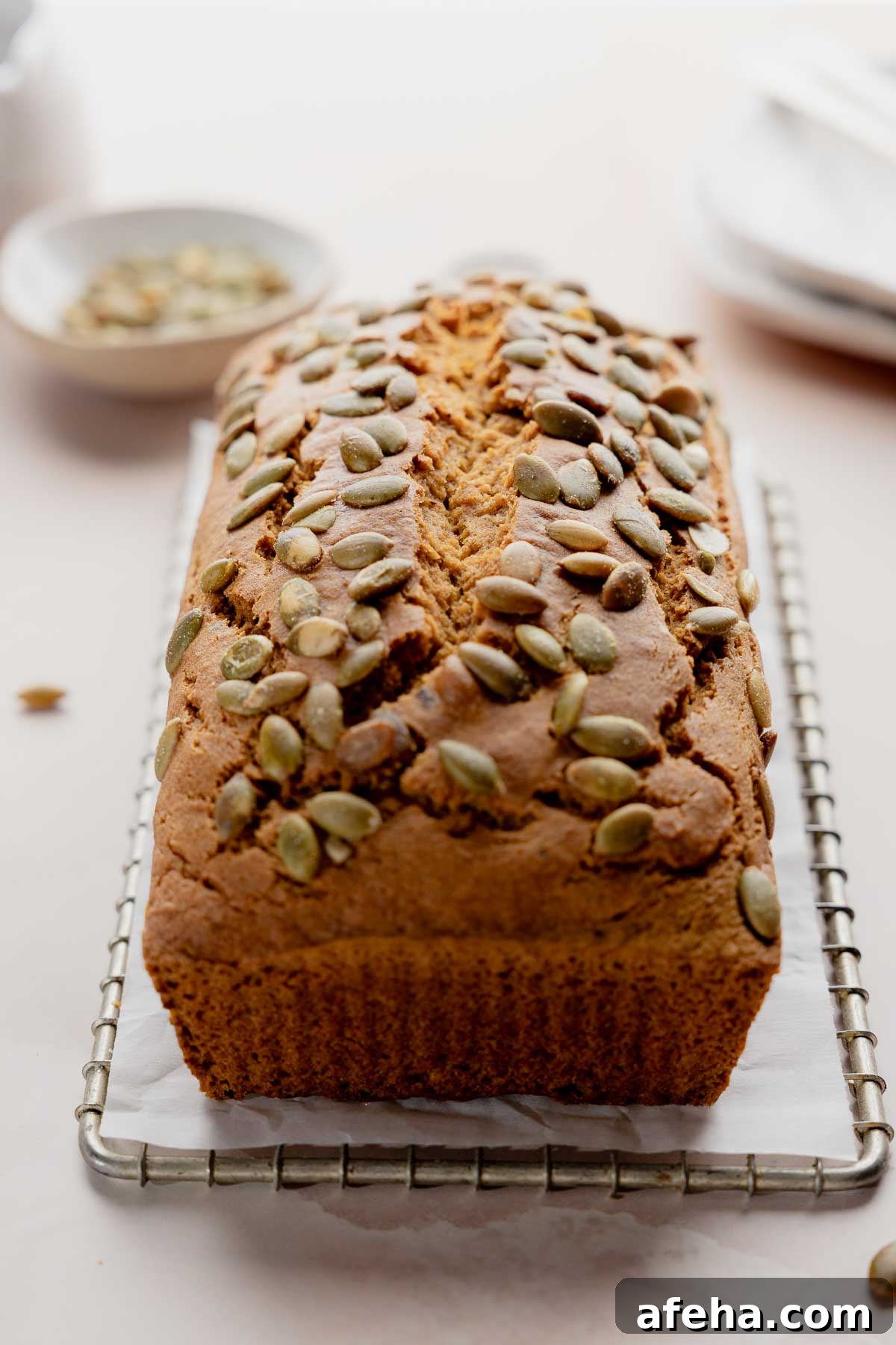 Baked gluten free pumpkin bread loaf topped with pumpkin seeds on cooling rack.