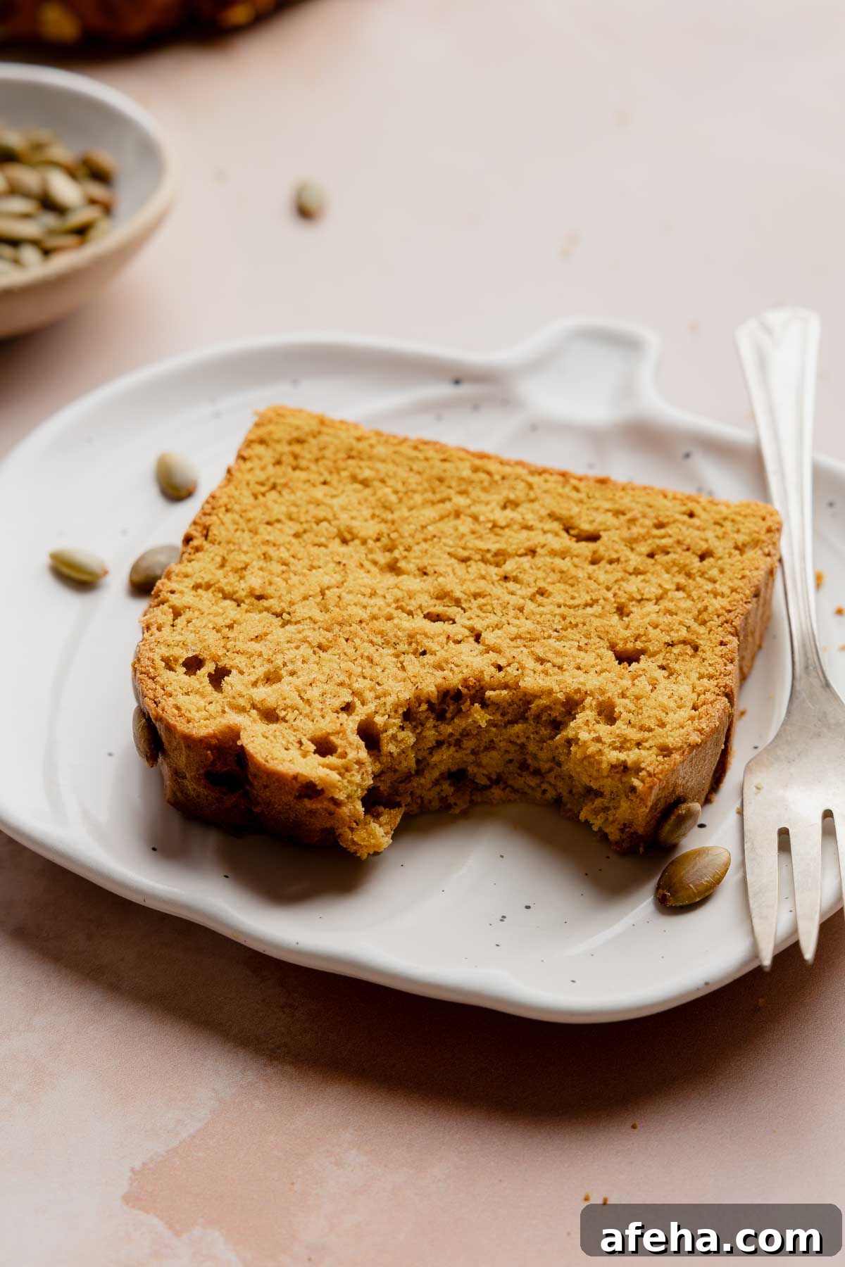 Slice of gluten free pumpkin bread with a bite taken out on white plate with fork.