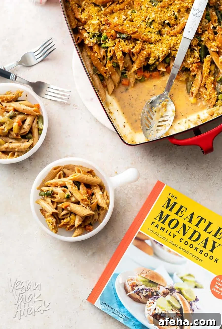 A photo of two bowls filled with vegan noodle casserole, next to a casserole dish and cookbook.