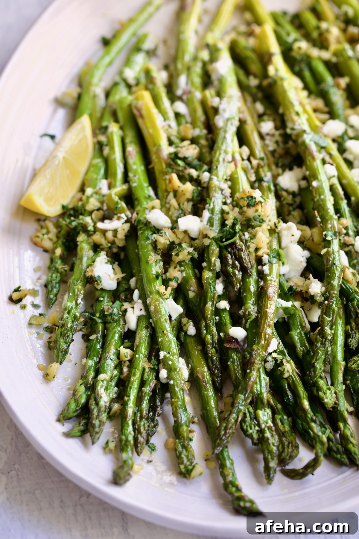 Roasted Asparagus with Walnut Lemon Gremolata and Goat Cheese on white oval platter with lemon wedge.