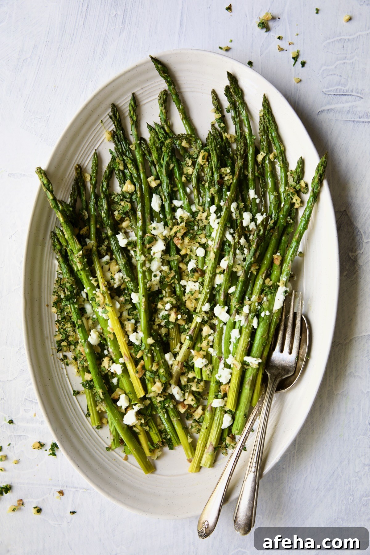 Roasted Asparagus with Walnut Lemon Gremolata and Goat Cheese on white oval platter.